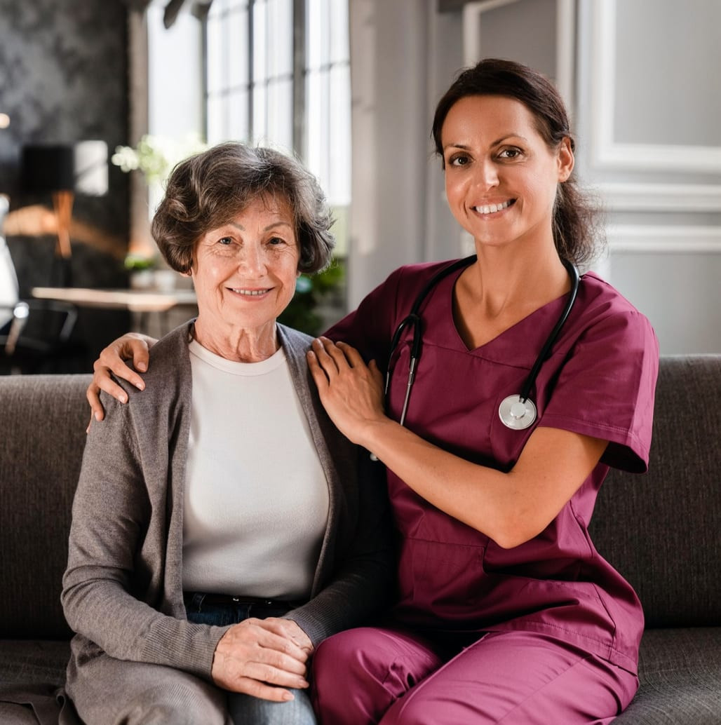 A nurse with her arm around an older woman on a sofa